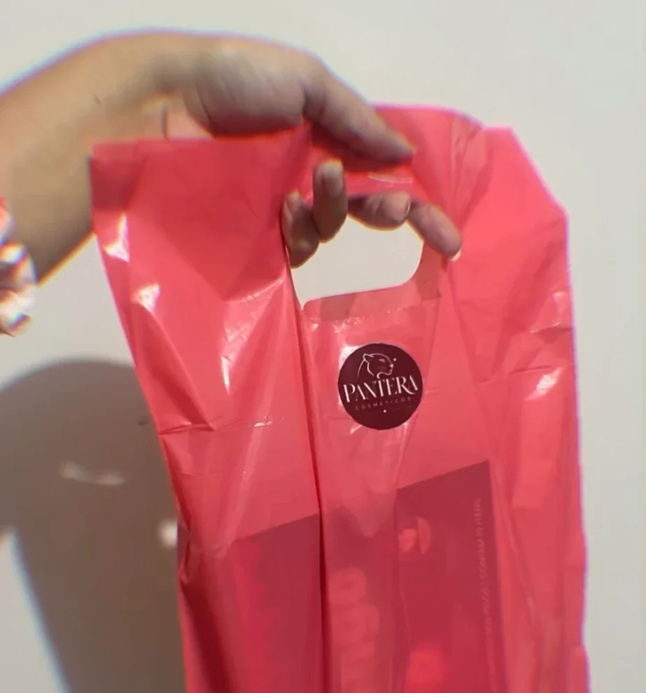 Mão segurando a sacola rosa da Pantera Cosméticos com o adesivo redondo do logo